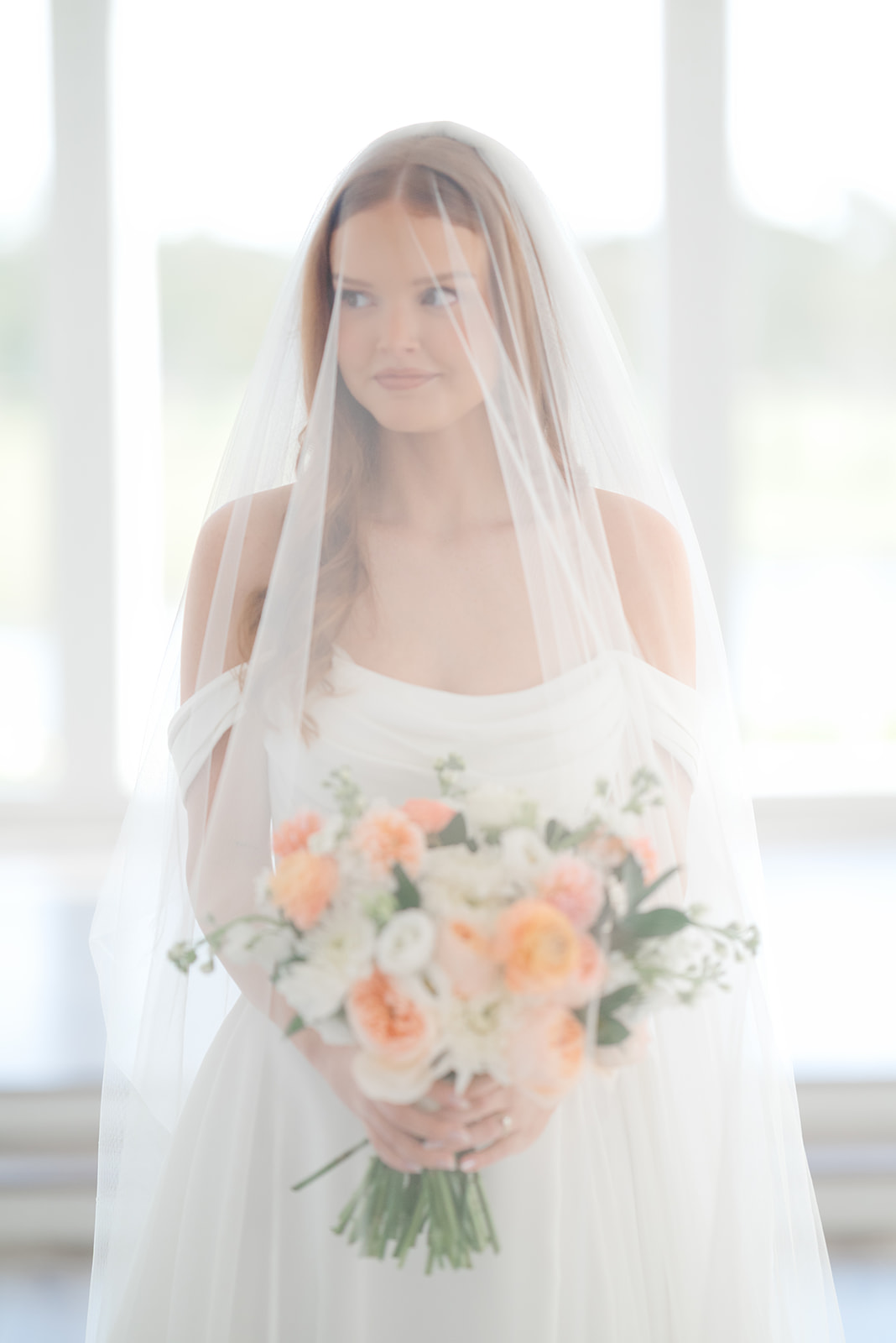 Bride wears veil over face with colorful wedding bouquet